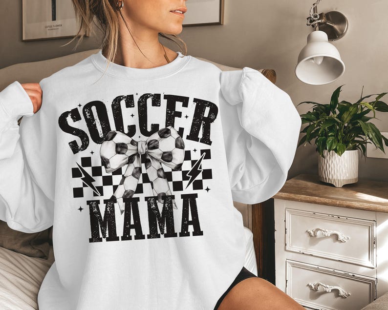Puede incluir: Sudadera blanca con texto negro que dice "Soccer Mama" con un patr&oacute;n de cuadros blanco y negro y un lazo de bal&oacute;n de f&uacute;tbol.