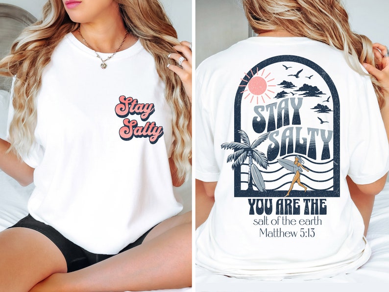 May include: White t-shirt with a retro-style graphic on the front that says "Stay Salty". The back of the shirt features a beach scene with a palm tree, sun, and waves. The text "Stay Salty" is also on the back, along with the words "You are the salt of the earth Matthew 5:13".