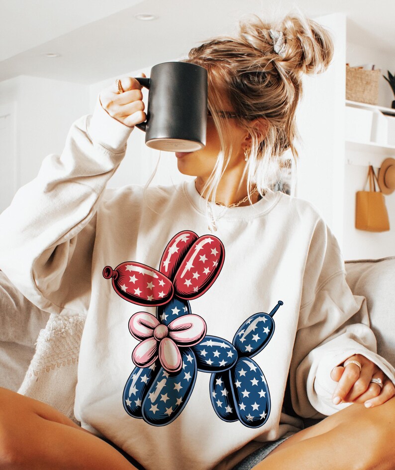 May include: A white sweatshirt with a red, white, and blue balloon animal design. The balloon animal is shaped like a dog and has stars on it.