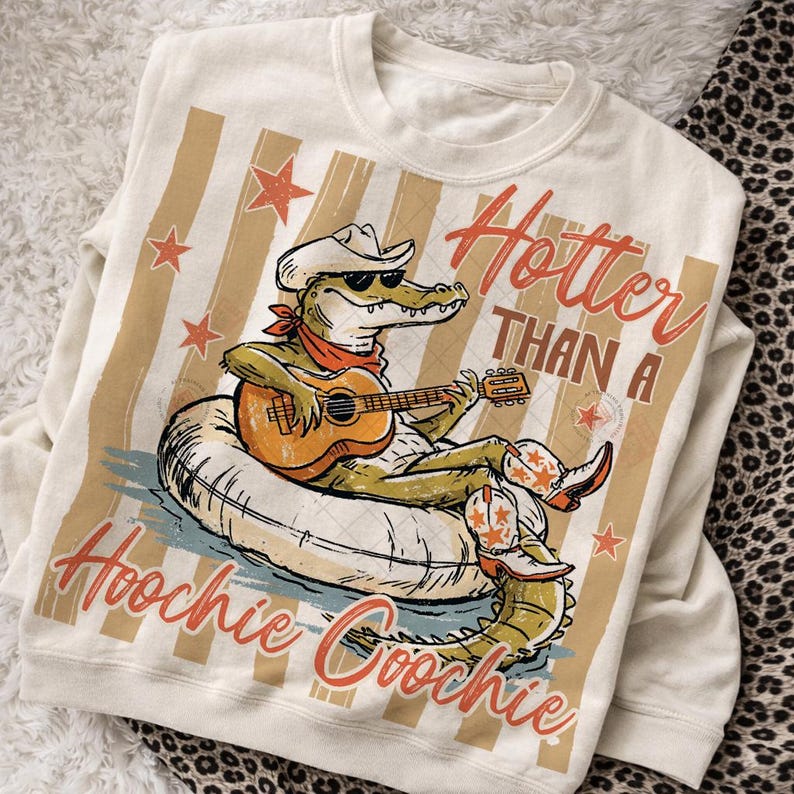 May include: Cream-colored sweatshirt with a graphic of an alligator wearing a cowboy hat and sunglasses, playing a guitar while floating on an inner tube. Text reads "Hotter Than A Hoochie Coochie."