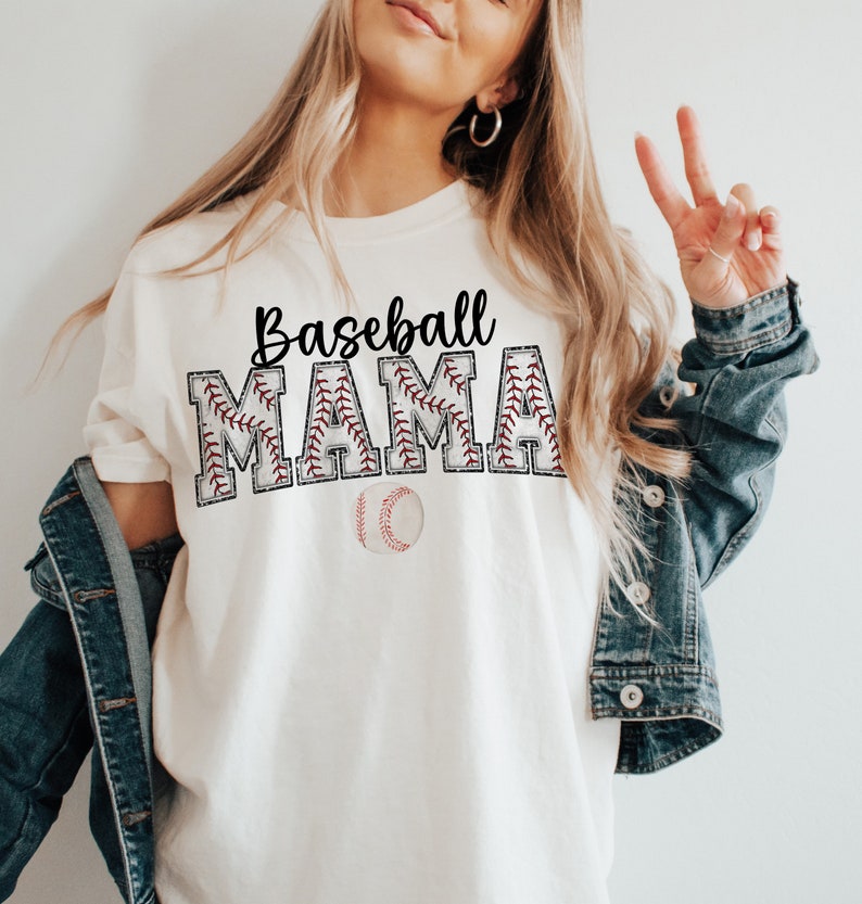 May include: White t-shirt with the text "Baseball Mama" in black lettering with a red baseball stitch design. A white baseball with red stitching is below the text.