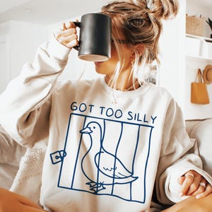 May include: A white sweatshirt with a blue graphic of a duck in a cage and the text "GOT TOO SILLY".