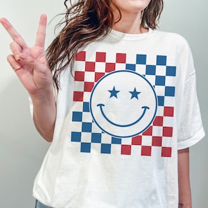 Op de afbeelding: Wit T-shirt met een blauw-rood geruit patroon en een witte smiley met twee sterren als ogen.