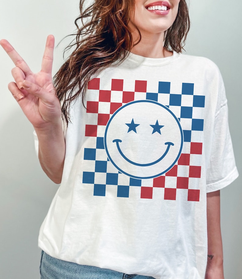 Op de afbeelding: Wit T-shirt met een blauw-rood geruit patroon en een witte smiley met twee sterren als ogen.