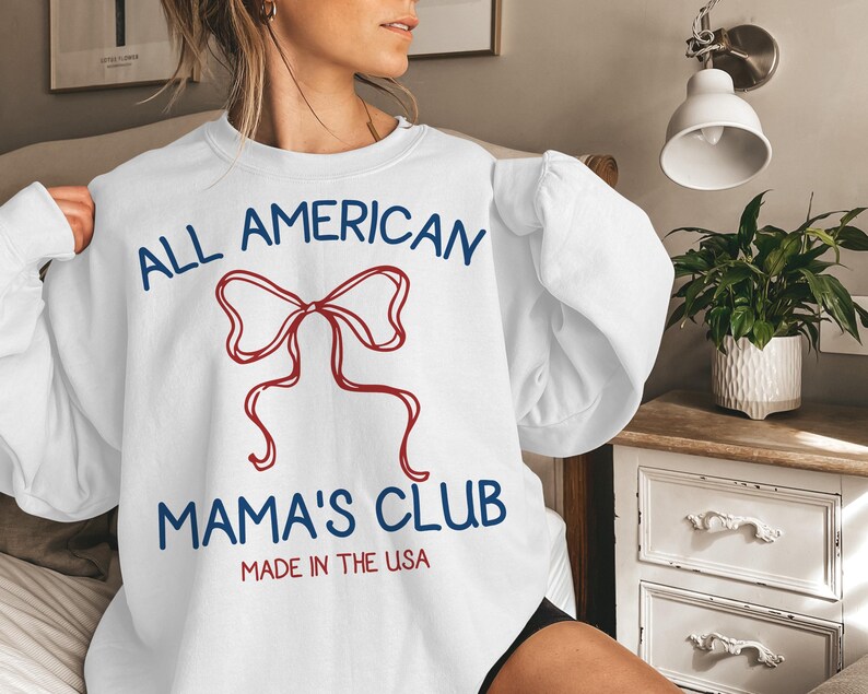 May include: White sweatshirt with the text "ALL AMERICAN MAMA'S CLUB" in blue and red, featuring a red bow graphic. The words "MADE IN THE USA" are printed below the club name.