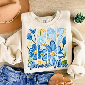 May include: A cream-colored sweatshirt with a graphic of blue and yellow flowers and the text "Summer Vibes".