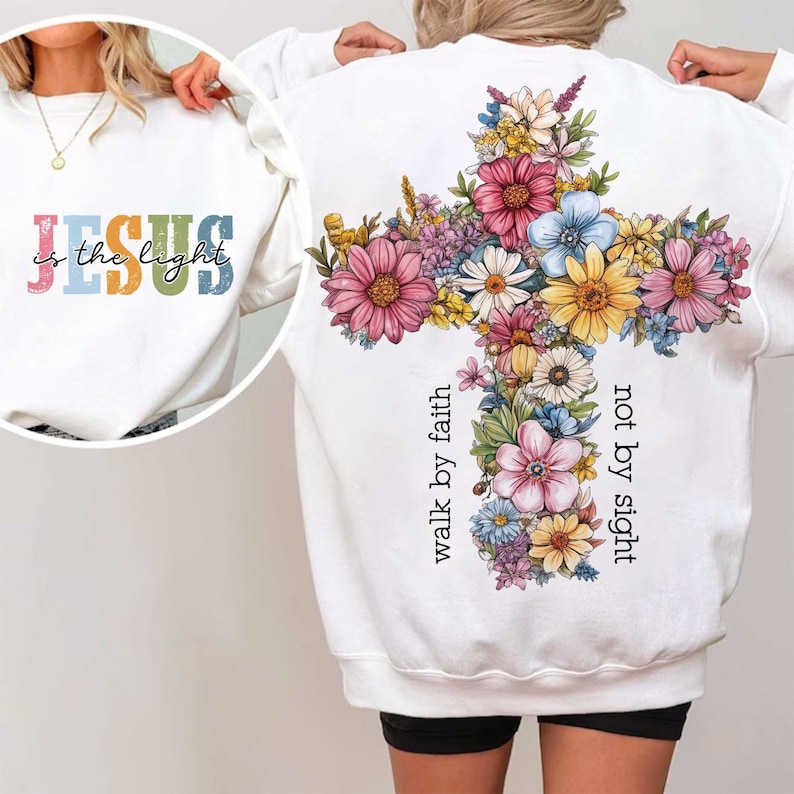 May include: White sweatshirt with the text "JESUS is the light" in colorful letters on the front. The back features a floral cross design with the words "walk by faith, not by sight" in black.