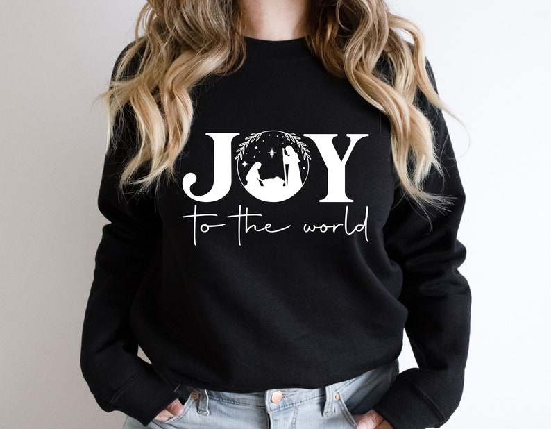Pu&ograve; includere: Felpa nera con testo bianco che recita "JOY to the world" con un'immagine stilizzata della scena della Nativit&agrave; all'interno della lettera "O".