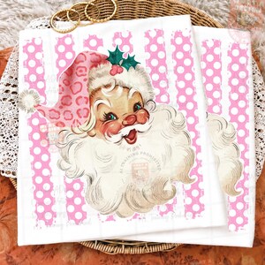 Pode incluir: Uma t-shirt branca com um gr&aacute;fico de um Pai Natal de estilo vintage, usando um gorro com padr&atilde;o de leopardo cor-de-rosa e um ramo de azevinho verde. O fundo do gr&aacute;fico consiste em riscas verticais cor-de-rosa com bolas brancas.