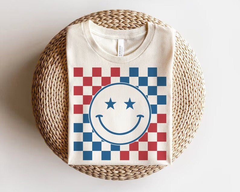 Op de afbeelding: Een wit T-shirt met een rood-blauw geruit patroon en een blauwe smiley met twee sterren boven de ogen.