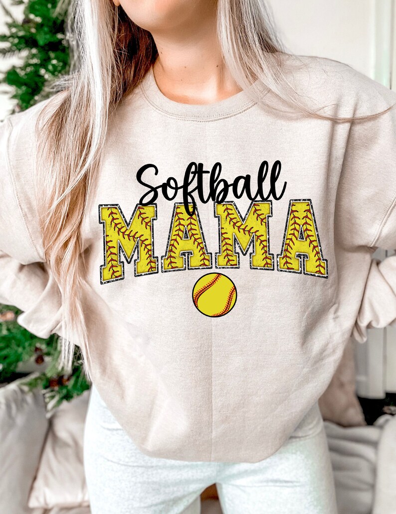 May include: A beige sweatshirt with the text "Softball Mama" in black and yellow. The text is surrounded by a yellow softball with red stitching.