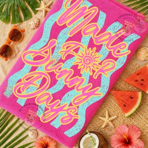 May include: A bright pink beach towel with the words "Make Sunny Days" in a wavy design. The text is in yellow and pink, with blue wavy lines. The towel is surrounded by beach-themed items like sunglasses, watermelon, and seashells.