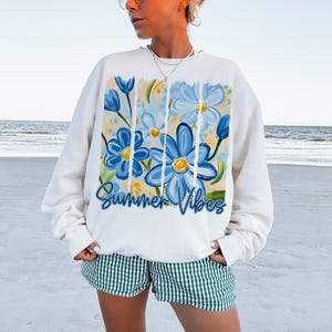 May include: White sweatshirt with a blue and yellow floral design and the text "Summer Vibes".