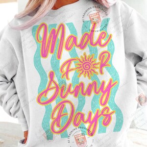 May include: White sweatshirt with the text "Made For Sunny Days" in pink and yellow script. The design includes a yellow sun graphic and turquoise wavy lines. A casual, summery style.
