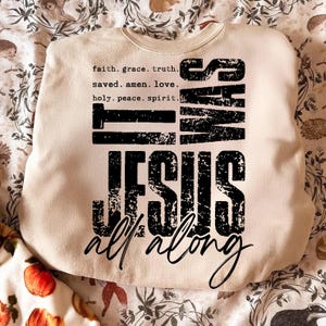 May include: Cream-colored sweatshirt with the text "IT WAS JESUS all along" in a distressed black font. The top includes a list of words like "faith, grace, truth" and "saved, amen, love". The sweatshirt is a casual, comfortable style.