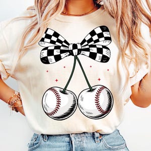 May include: A white t-shirt with a black and white checkered bow tied around two cherries. The cherries are shaped like baseballs with red stitching.