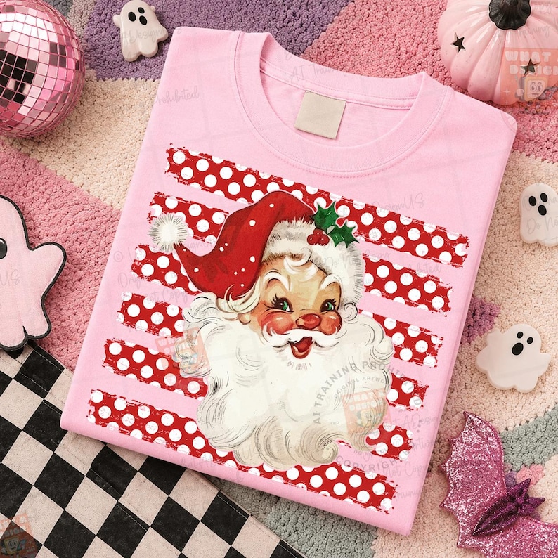 May include: A light pink t-shirt featuring a graphic of a vintage-style Santa Claus with a red hat and white beard, centered over horizontal stripes of red and white polka dots. The design includes a small green holly sprig on the hat.