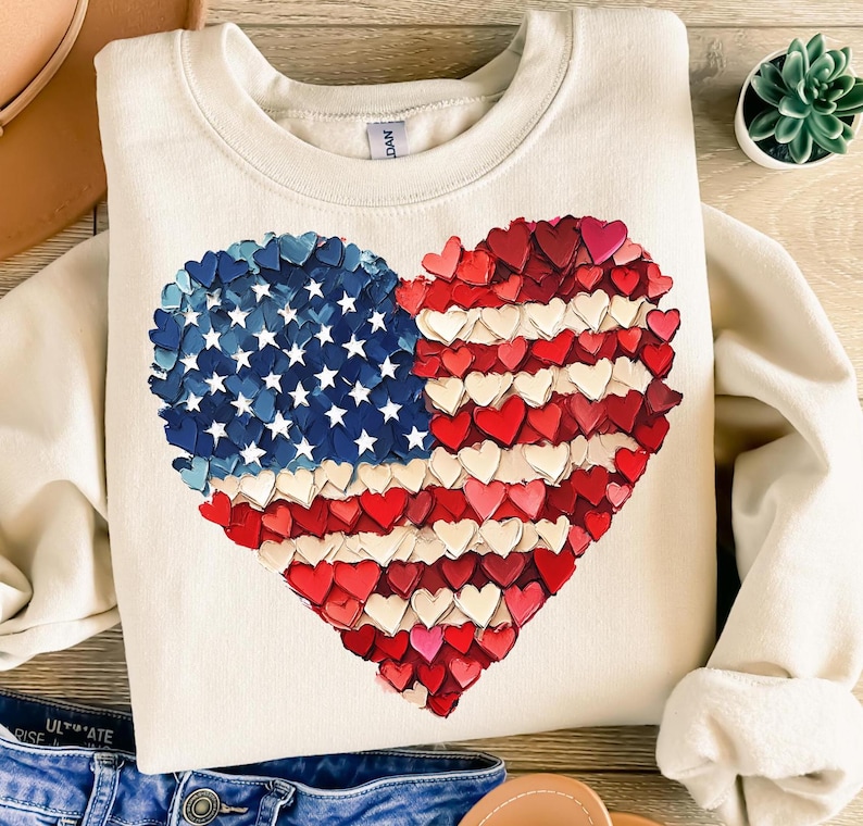 May include: A cream-colored sweatshirt with a large heart-shaped American flag design. The flag is made up of small red, white, and blue hearts.