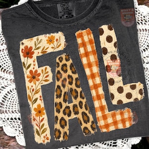 May include: A charcoal gray t-shirt featuring the word FALL in large block letters. Each letter has a distinct pattern: the F is floral with orange flowers, the A is leopard print, the L is orange gingham, and the second L is brown polka dots.