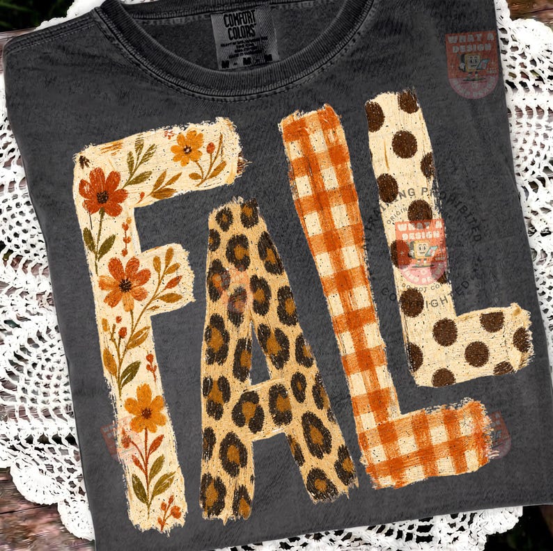 May include: A charcoal gray t-shirt featuring the word FALL in large block letters. Each letter has a distinct pattern: the F is floral with orange flowers, the A is leopard print, the L is orange gingham, and the second L is brown polka dots.
