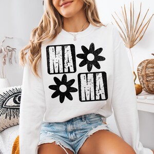Peut inclure: Sweat-shirt blanc avec un imprim&eacute; graphique noir du mot "MAMA" avec des fleurs stylis&eacute;es de chaque c&ocirc;t&eacute;.