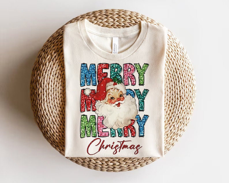 Op de afbeelding: Een wit T-shirt met een vintage-stijl illustratie van de kerstman en de woorden "Merry Christmas" in kleurrijke, glinsterende letters.