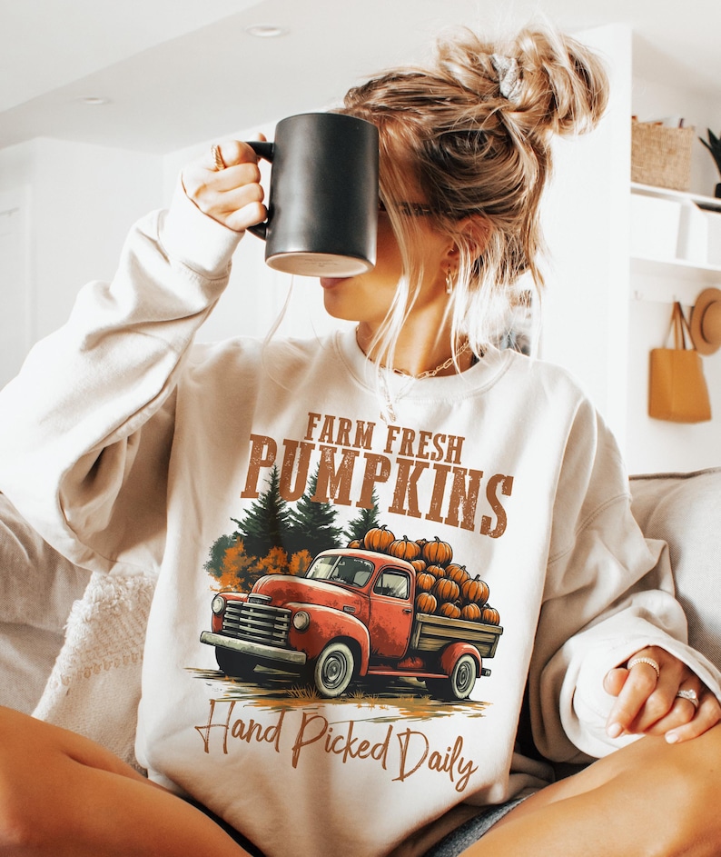 Op de afbeelding: Een wit sweatshirt met een vintage truck-ontwerp. De truck is rood en heeft een laadbak vol pompoenen. De tekst op het sweatshirt luidt "Farm Fresh Pumpkins Hand Picked Daily".