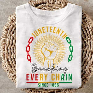 Peut inclure: T-shirt blanc avec un motif graphique repr&eacute;sentant un poing lev&eacute; brisant une cha&icirc;ne. Le texte "Juneteenth" est en cercle autour du poing, et le texte "Breaking Every Chain Since 1865" est sous le poing.