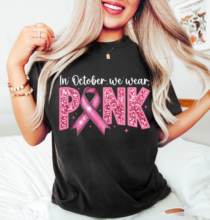 May include: Black t-shirt with the text "In October we wear PINK" in pink glitter letters with a pink ribbon in the center.