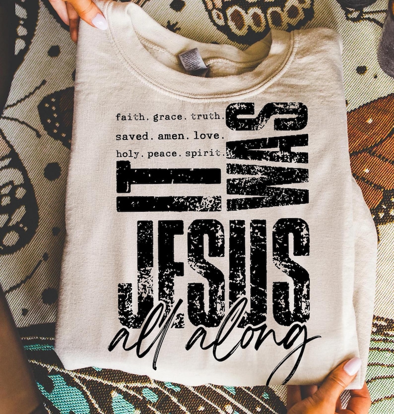 May include: A folded, cream-colored sweatshirt with the text "IT WAS JESUS all along" in black. The top text includes the words "faith, grace, truth, saved, amen, love, holy, peace, spirit."