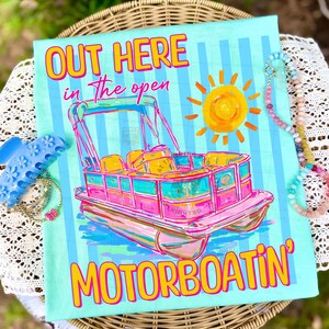 May include: A light blue t-shirt with a colorful illustration of a pontoon boat, a yellow sun, and the text "OUT HERE in the open MOTORBOATIN'". The shirt is decorated with vertical blue stripes.