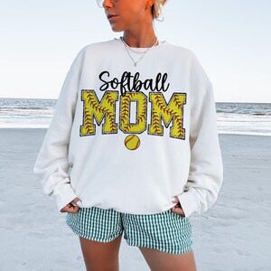May include: White sweatshirt with the text "Softball MOM" in black and yellow. The letters are outlined in red and have a softball pattern.