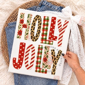 Op de afbeelding: Een wit rechthoekig canvasbord met de tekst HOLLY JOLLY in grote blokletters. Elke letter heeft een ander patroon, waaronder rode kerststerren, luipaardprint, rood-groene ruiten, rode stippen en rood-witte strepen.