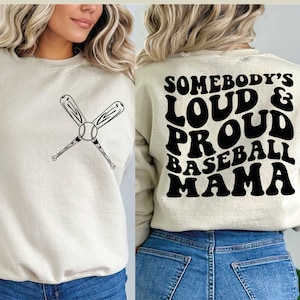 May include: A beige sweatshirt with a baseball and crossed bats graphic on the front and the text "Somebody's Loud & Proud Baseball Mama" on the back.