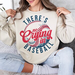 Peut inclure: Un sweat-shirt cr&egrave;me avec un graphique de baseball vintage et le texte "There's no crying in baseball".