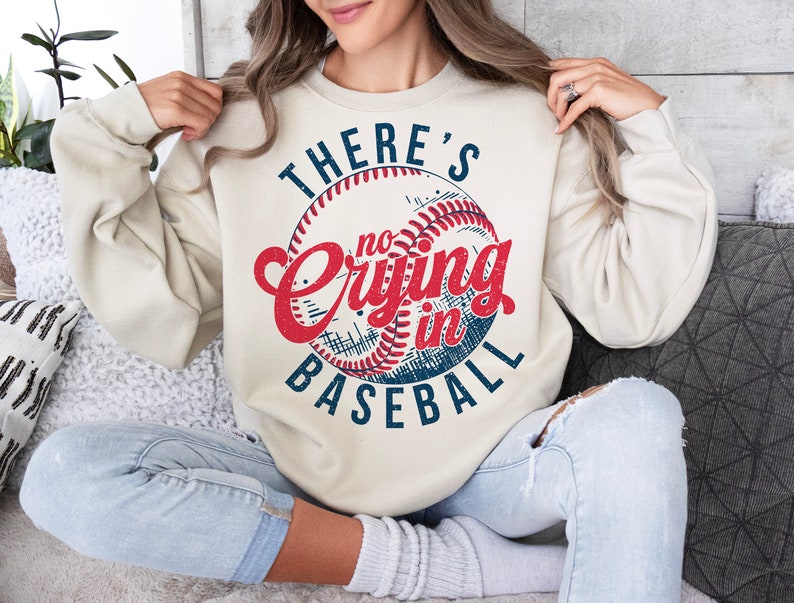 Peut inclure: Un sweat-shirt cr&egrave;me avec un graphique de baseball vintage et le texte "There's no crying in baseball".