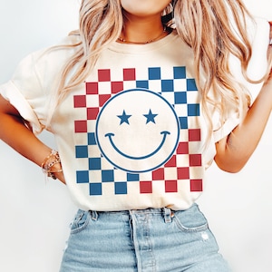 Op de afbeelding: Een wit T-shirt met een rood-blauw geruit patroon en een blauwe smiley met twee sterren als ogen.