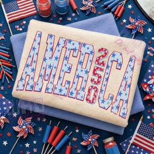 May include: A cream-colored rectangular item with the word "AMERICA 250" in red and blue stars. The item is on top of a blue blanket, surrounded by patriotic decorations, including flags and pinwheels.