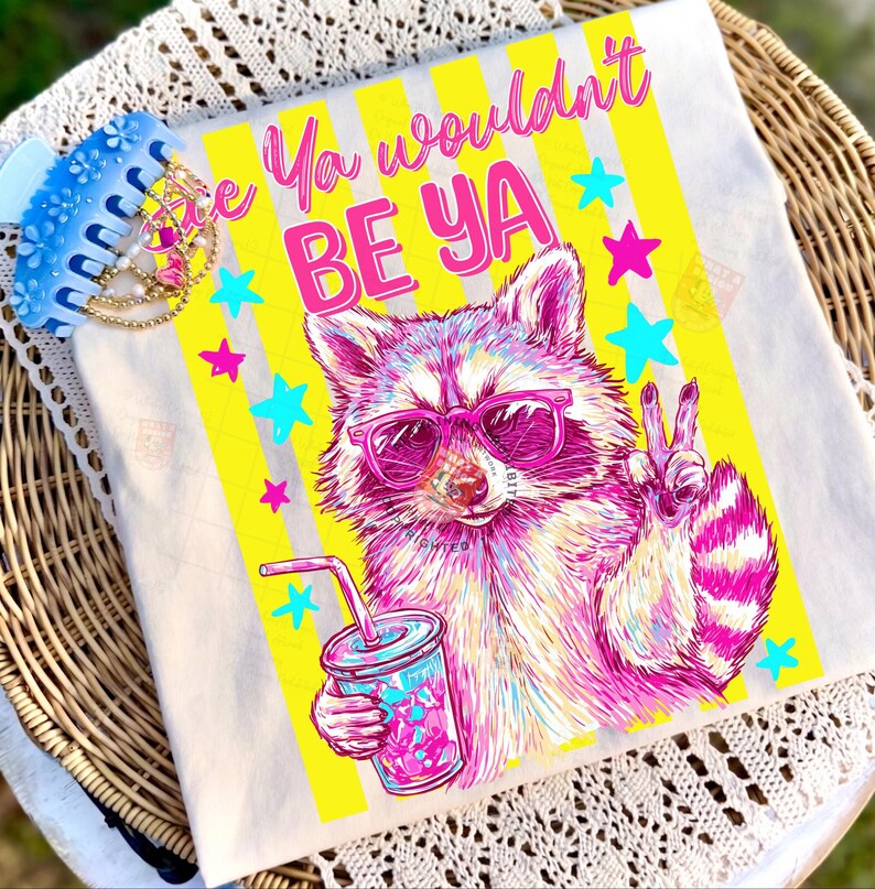 Peut inclure: Un t-shirt blanc avec un motif color&eacute; d'un raton laveur portant des lunettes de soleil roses et tenant une boisson. Le t-shirt porte l'inscription "Ya wouldn't BE YA" avec des rayures jaunes et des &eacute;toiles. Une pince &agrave; cheveux bleue est visible.