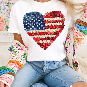 May include: White t-shirt with a red, white, and blue heart-shaped American flag design made of small hearts.