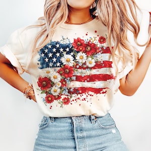 May include: A white t-shirt with a watercolor design of the American flag with red, white, and blue flowers.