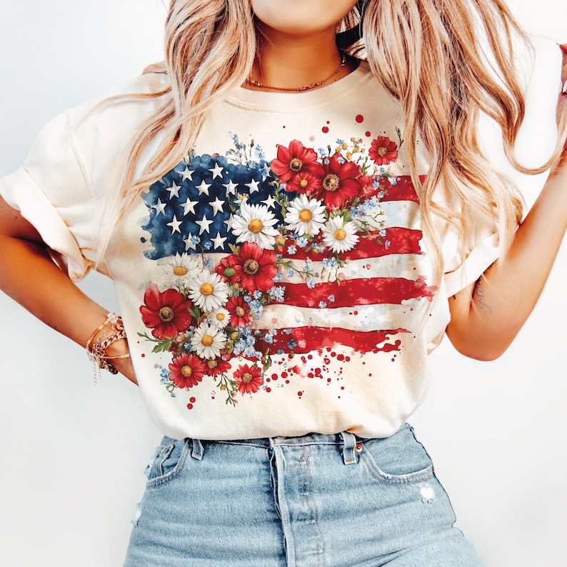 May include: A white t-shirt with a watercolor design of the American flag with red, white, and blue flowers.