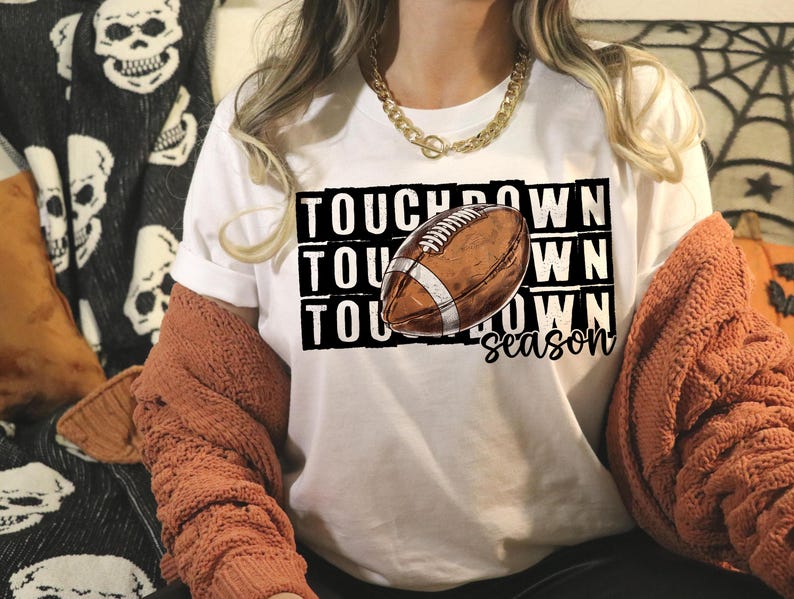 Op de afbeelding: Wit T-shirt met de tekst "Touchdown Season" en een afbeelding van een bruine en witte voetbal.