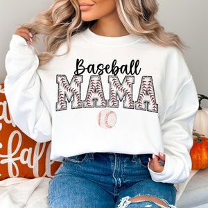 May include: White sweatshirt with the text "Baseball Mama" in black with red stitching on the letters. A white baseball is below the text.