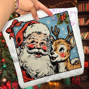 May include: White Christmas-themed pillow featuring a vintage illustration of Santa Claus and a reindeer. Santa is wearing a red hat and has a long white beard. The reindeer has brown fur and antlers. The background is light blue with snowflakes.