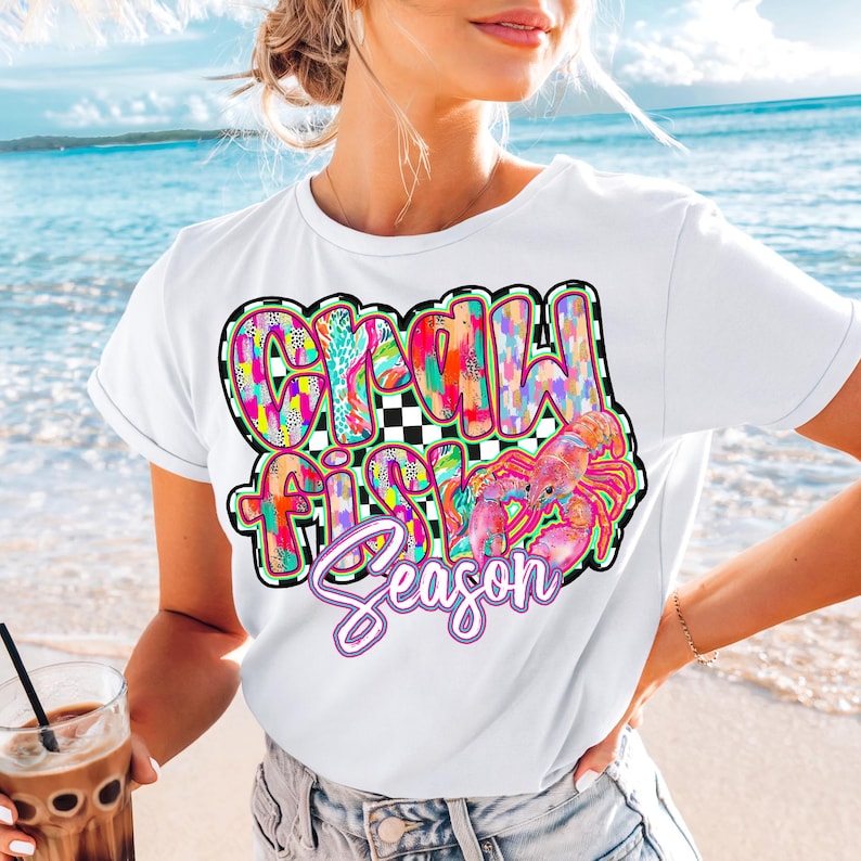 May include: White t-shirt with a colorful graphic that says "Crawfish Season" with a pink crawfish illustration.