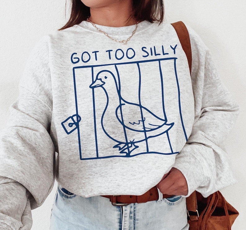 May include: A gray sweatshirt with the text "GOT TOO SILLY" printed on the front. The text is in a blue font and is surrounded by a blue outline of a bird in a cage.