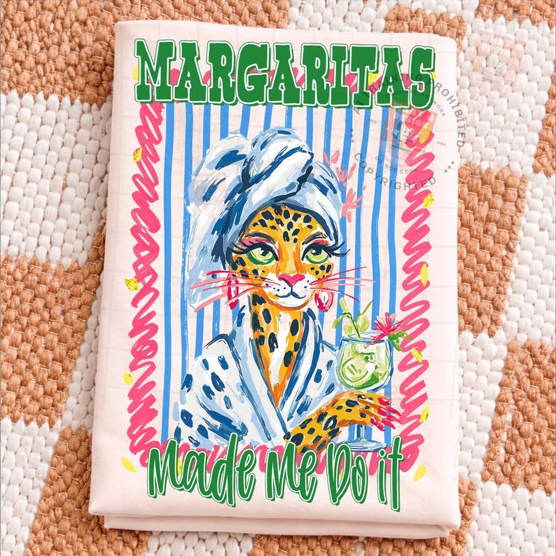 Pu&ograve; includere: Un asciugamano rosa chiaro con un'illustrazione di leopardo con un accappatoio e un margarita. L'asciugamano ha le parole "Margaritas" e "Made Me Do It" in testo verde, con accenti a strisce blu e rosa.
