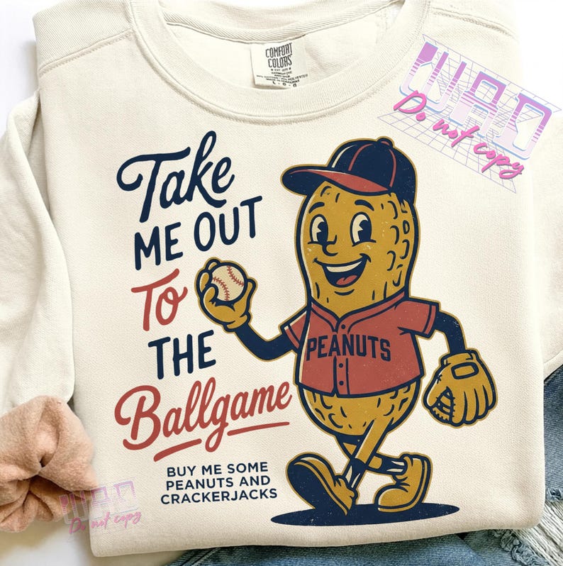 May include: Cream-colored sweatshirt with a baseball-themed graphic. The design features a smiling peanut character in a baseball uniform holding a baseball, with the text "Take Me Out To The Ballgame".