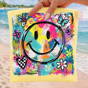 May include: A yellow square-shaped item with a large, black smiley face at the center. The face is surrounded by colorful abstract paint strokes in pink, blue, yellow, and green. Floral and butterfly designs are also present.